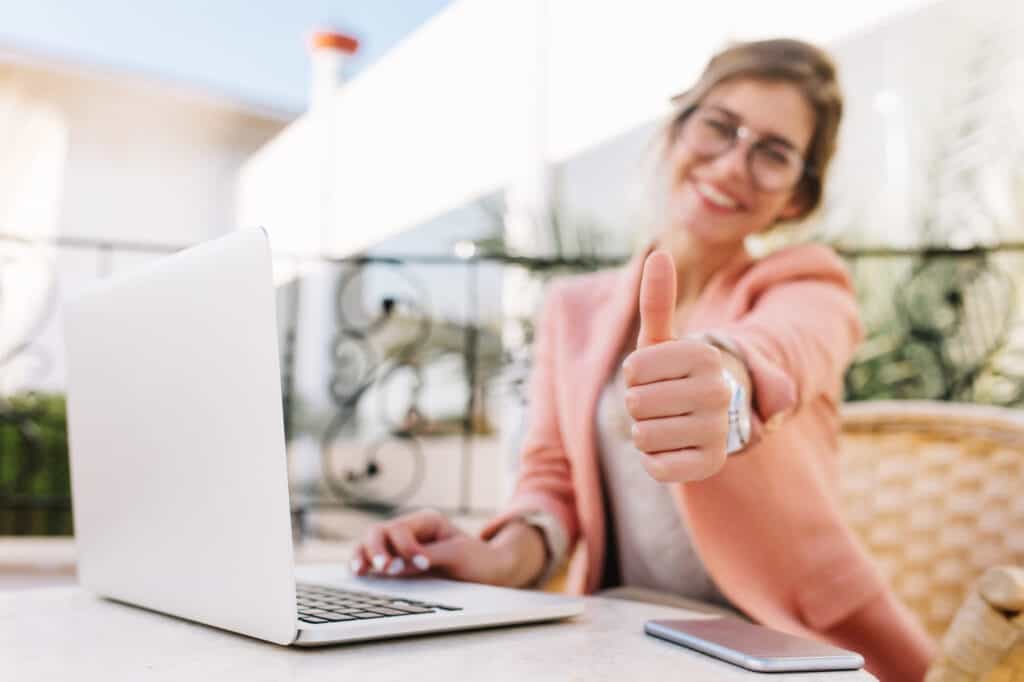Une jeune femme contente montre le pouce vers le haut devant un ordinateur